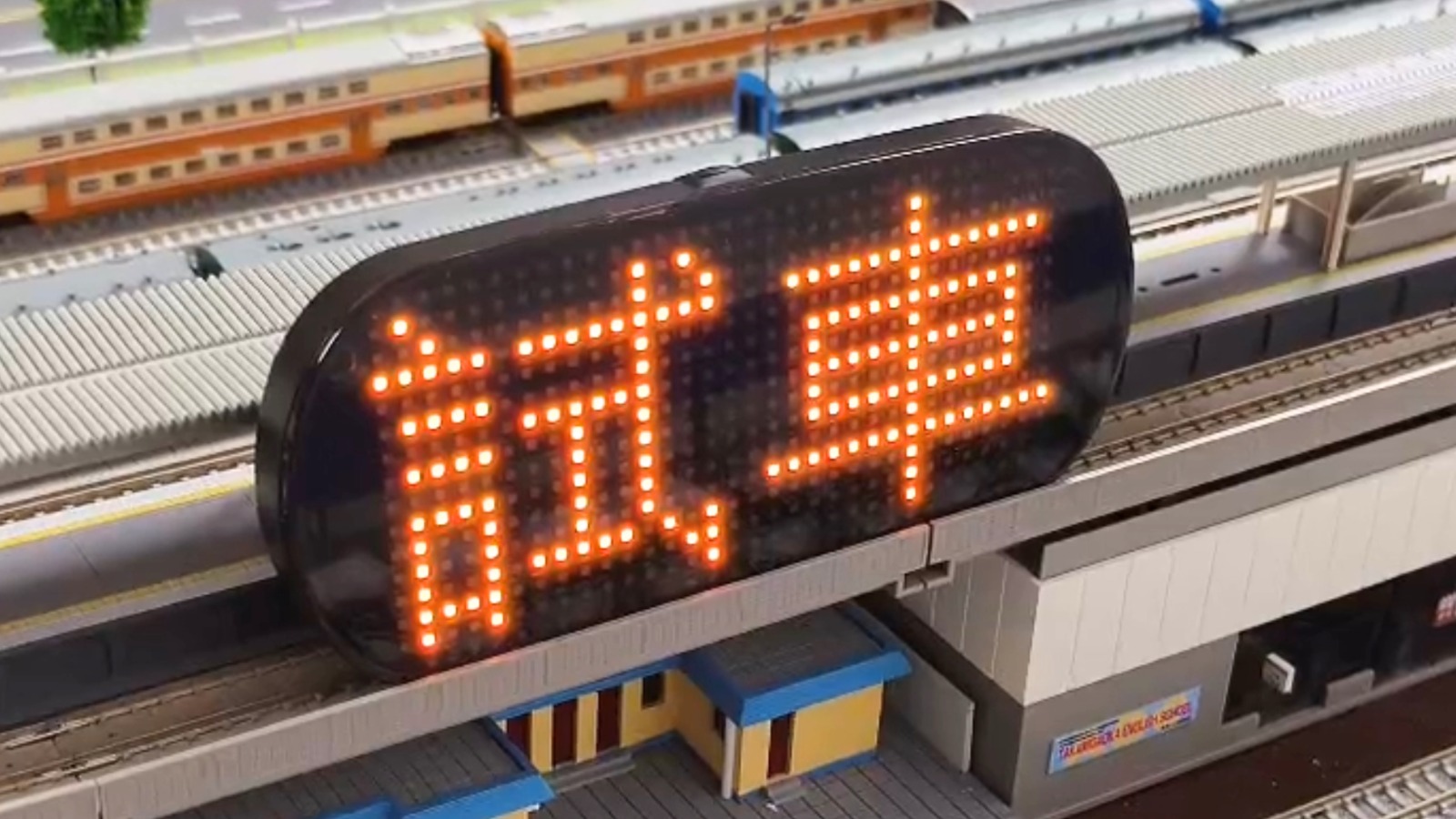 运动屏 Lite 悬挂在火车站沙盘模型场景中，橙色点阵文字显示"試車"